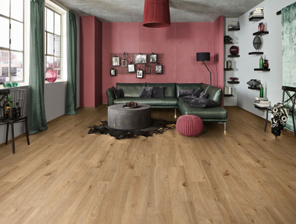 Modernes Wohnzimmer mit grünem Sofa, rotem Sessel und Laminatboden der Serie 'Vinto'. Wand in Rosa, Regale mit Dekorationen, große Fenster.