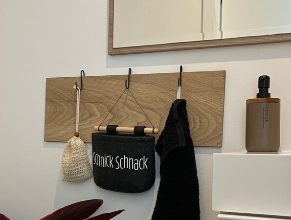 Spiegel über Wandhaken mit Tasche und Handtuch, Pflanze im Vordergrund.