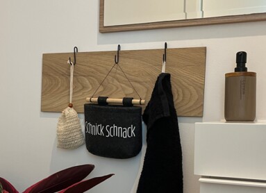 Spiegel über Wandhaken mit Tasche und Handtuch, Pflanze im Vordergrund.