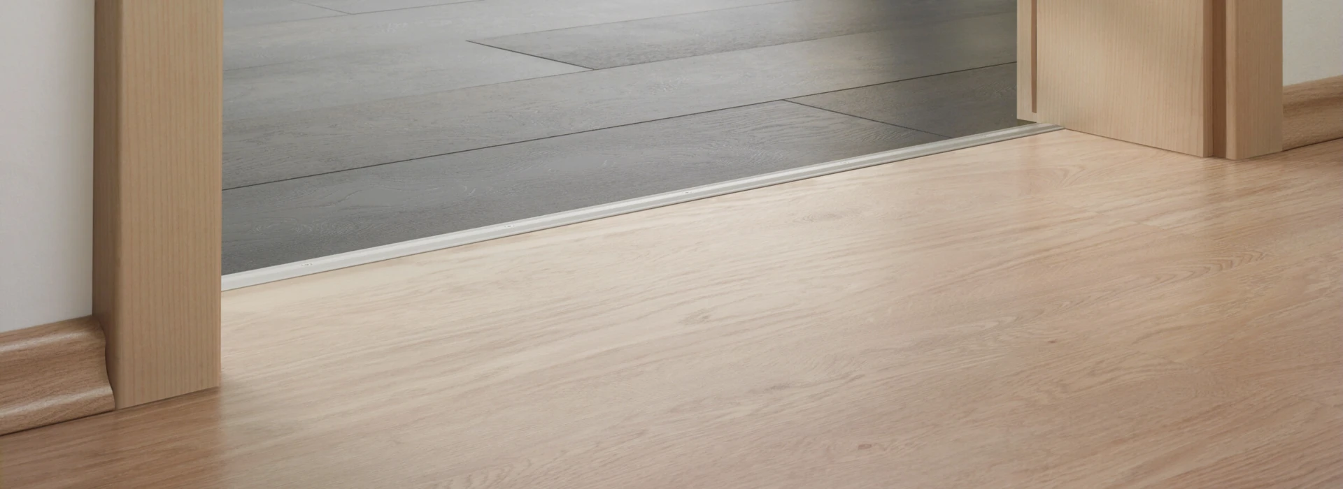 Blick von einem Raum mit hellem Laminatboden in einen Bereich mit dunklem Bodenbelag und Dekoration.