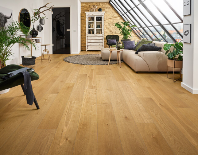 A bright living room with elegant laminate flooring, a beige sofa, plants, and a slanted glass window.