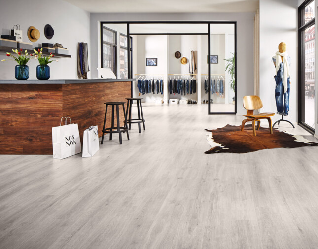 Moderner Raum mit hellem Laminatboden, Holztresen, Schaufenster und Kleiderständer.