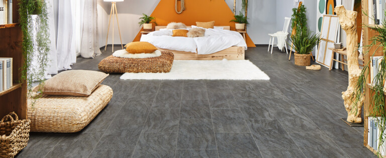 Gemütliches Schlafzimmer mit grauem Laminatboden der Serie 'Ceramico', orangefarbener Wand und natürlichen Dekorationen.