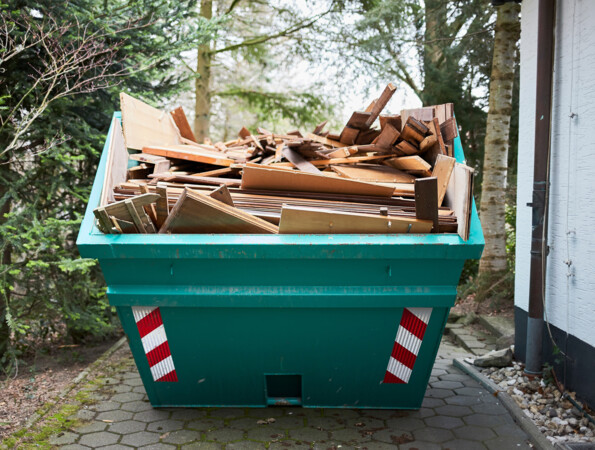 Ein großer Container gefüllt mit alten Laminatbodenstücken steht im Freien neben einem Gebäude.