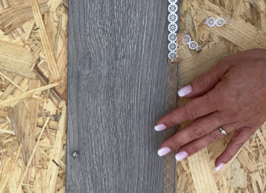 Hand verziert graues Laminatbrett mit Spitzenband auf Spanplatte.