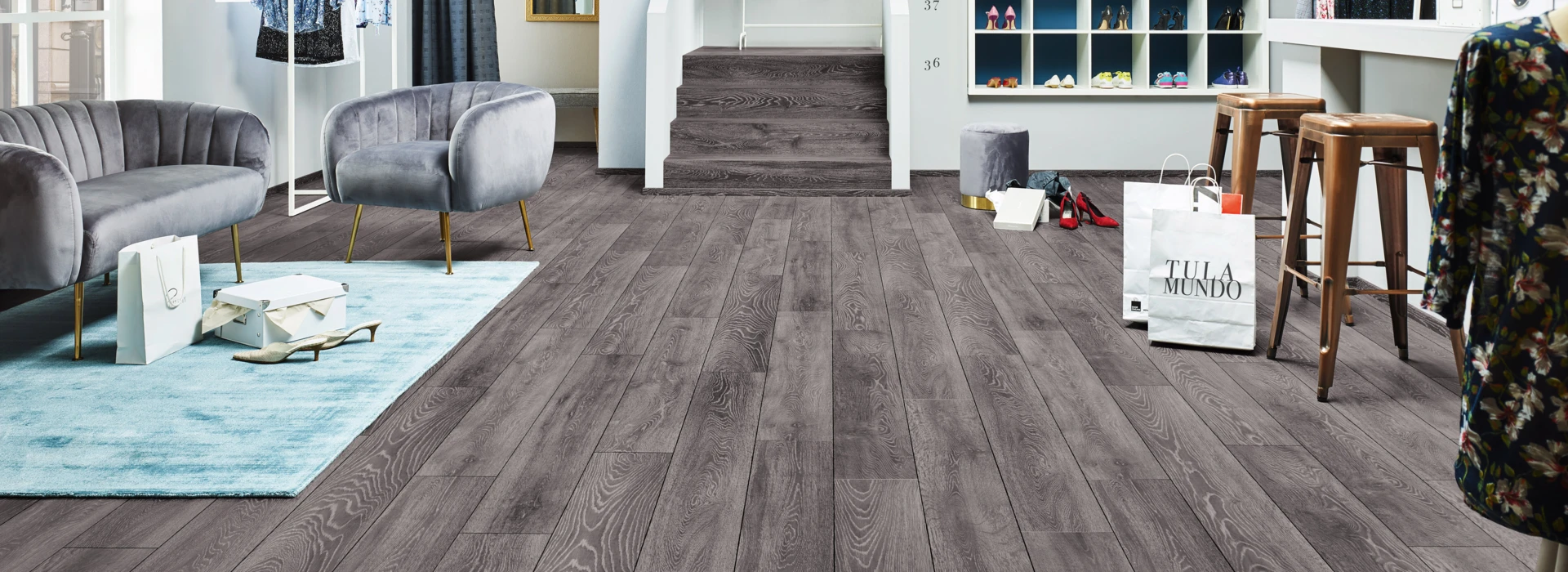 Contemporary boutique with grey laminate flooring, stylish seating, and clothing displays, showcasing a chic and inviting shopping environment.