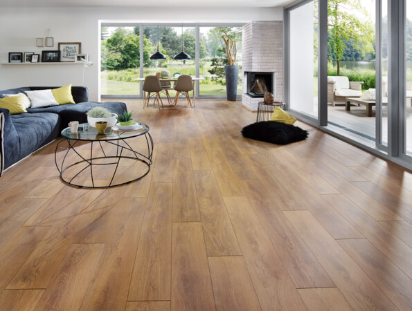Spacious living room with light laminate flooring, large windows, and a cosy seating area overlooking a garden.