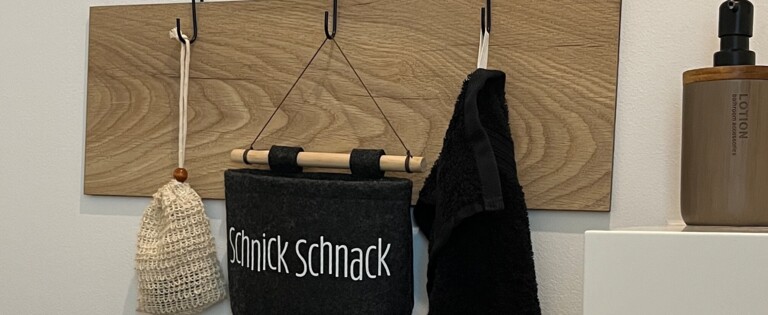 Spiegel über Wandhaken mit Tasche und Handtuch, Pflanze im Vordergrund.
