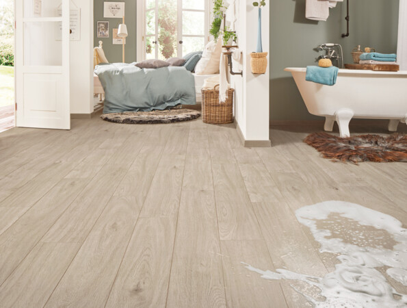 Open living space with light laminate flooring, featuring a cosy bed area and a classic bathtub, complemented by soft natural light.