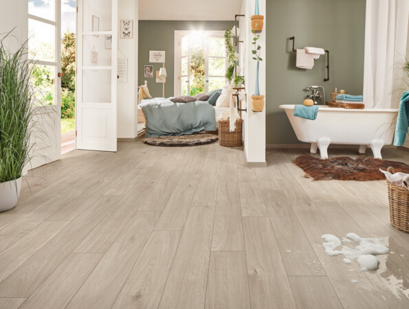 Helles Badezimmer mit freistehender Badewanne und Laminatboden, angrenzend an ein Schlafzimmer mit offener Tür zum Garten.