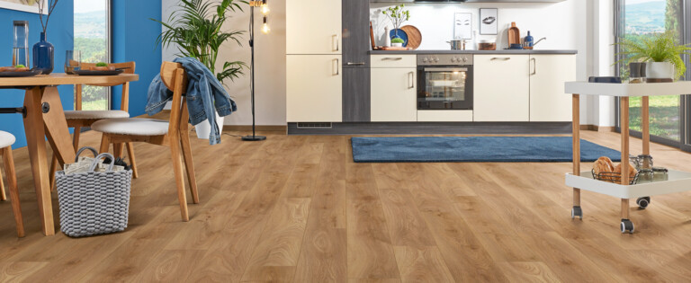 Moderner Küchen- und Essbereich mit hellem Laminatboden der Serie 'Aquaprotect Smart Silent' und blauer Wand, Holzmöbeln und großen Fenstern.