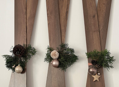 Drei dekorative Holzlatten mit Weihnachtsdeko aus Tannenzweigen und Kugeln an der Wand.