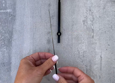 Eine Person hält einen schwarzen Uhrzeiger vor einer grauen Oberfläche.