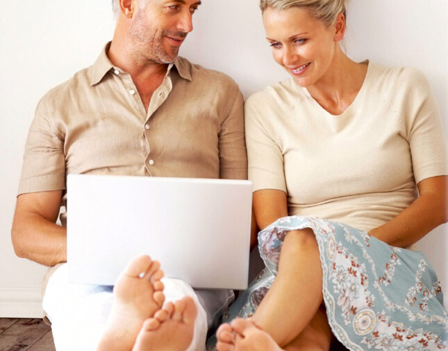 Couple sitting on laminate flooring, smiling at a laptop, enjoying a relaxed moment together.