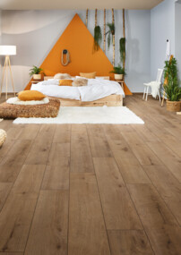 Gemütliches Schlafzimmer mit hellem Laminatboden, Bett, Pflanzen und dekorativen Details.