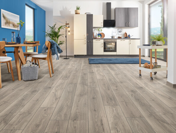 Küche mit hellem Laminatboden, Holztisch und blauem Akzent an der Wand, große Fenster für natürliches Licht.