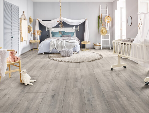 Helles Schlafzimmer mit grauem Laminatboden der Serie 'Vinto' und gemütlicher Dekoration, einschließlich Himmelbett, Babybett und Spielzeug.