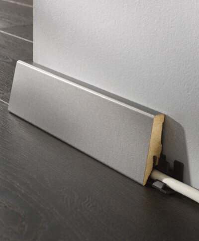 Sockelleiste aus Holz, die Kabel auf dunklem Laminatboden verdeckt.