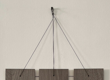 Wanddekoration mit Fotos und Karten auf Holzpaneelen, darunter ein Regal mit Keramikfigur und Stiftehalter.