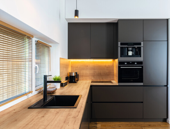 Moderne Küche mit Arbeitsplatte 'elementa', schwarzen Schränken, eingebautem Ofen und Laminatboden.