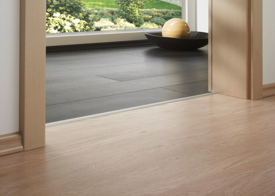 Laminate flooring in a bright room with garden view, featuring a smooth transition between different floor styles.