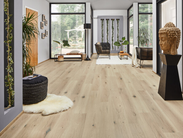 Heller Raum mit großen Fenstern, Pflanzen und einer Buddha-Statue; Laminatboden in Holzoptik.