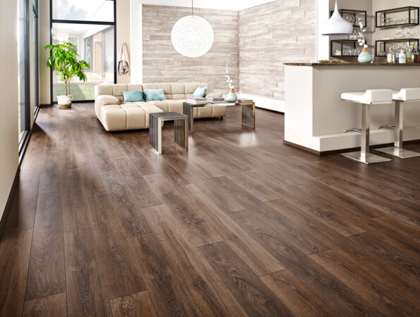 Helles Wohnzimmer mit dunklem Laminatboden, beigem Sofa, Barbereich und großen Fenstern.